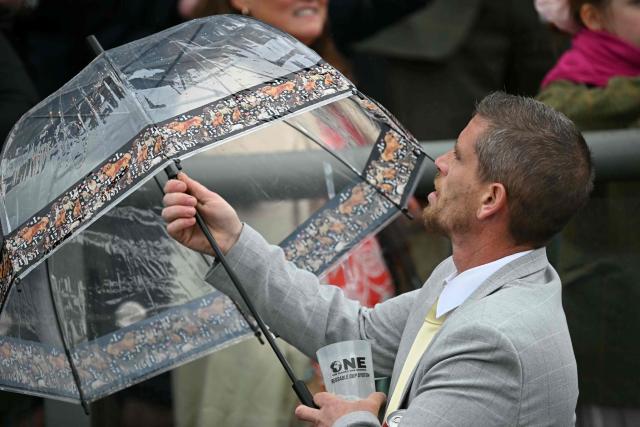 A man tries to open an umbrella on the opening day of the Grand National Festival horse race meeting at Aintree Racecourse in Liverpool, north-west England, on April 9, 2026. (Photo by Paul ELLIS / AFP)