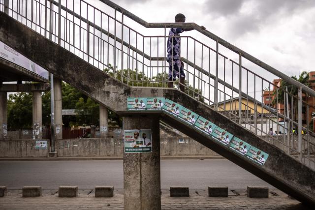 A resident walks on a bridge past election posters of Paul Hounkpe, presidential candidate of the Force Cauris pour un Benin Emergent (FCBE) party, in Cotonou on April 9, 2026, ahead of Benin's presidential election scheduled for April 12, 2026. (Photo by OLYMPIA DE MAISMONT / AFP)