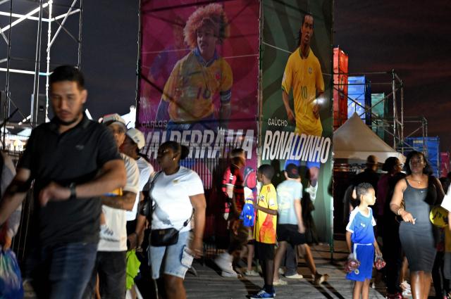 people walk near banners depicting formar footballers, Brazilian Ronaldinho Gaucho and Colombian Carlos Valderrama, during the Legends Football Tournament in Willemstad, Curacao, in the Dutch Caribbean, on April 8, 2026. (Photo by Raul ARBOLEDA / AFP)