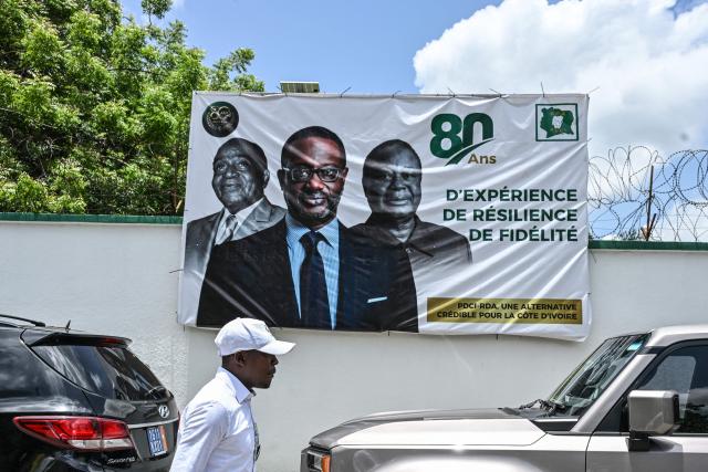 A man walks past Ivory Coast's Democratic Party (PDCI) banner featuring images of Ivory Coast's first President and founder of PDCI-RDA, Felix Houphouet-Boigny (L), former President Henri Konan Bedie (R) and party president Tidiane Thiam (C), during the celebration of PDCI-RDA's 80th anniversary at the party headquarters in Abidjan on April 9, 2026. (Photo by Issouf SANOGO / AFP)