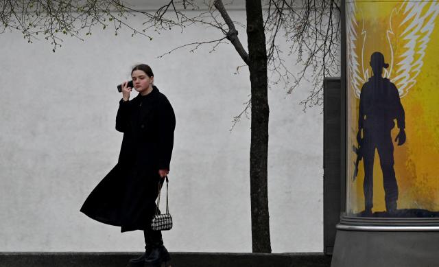 A pedestrian takes a phone call near a placard reading "The Armed Forces of Ukraine are our guardian angels" in Kyiv on April 9, 2026, amid Russian invasion in Ukraine. (Photo by Sergei SUPINSKY / AFP)