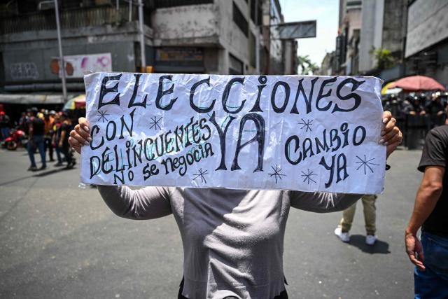 An opponents to the government of Venezuelan interim President Delcy Rodriguez demonstrates with a sign reading "Eelections now. We don´t negociate with criminals. Change now" in demand of salary and pension raises in Caracas on April 9, 2026. Venezuelan police fired tear gas to disperse around 2,000 protesters who marched towards the presidential palace to demand salary and pension increases, AFP reporters saw. (Photo by Juan BARRETO / AFP)