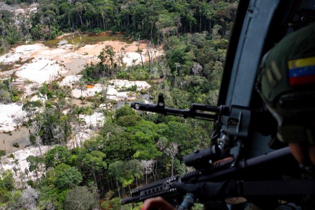 (FILES) Bolivarian National Armed Forces (FANB) General Ochoa and a female artillery look out from a Russian-made MI17 helicopter flying over the Yapacana National Park during the "Autana" military operation against illegal mining in Amazonas state, in the Venezuela-Colombia-Brazil border, on December 21, 2022. Venezuela's Parliament approved a mining law that opens the door for foreign investors to exploit the country's vast reserves on April 9, 2026, following a similar move regarding the oil industry under pressure from the United States. (Photo by Yuri CORTEZ / AFP)
