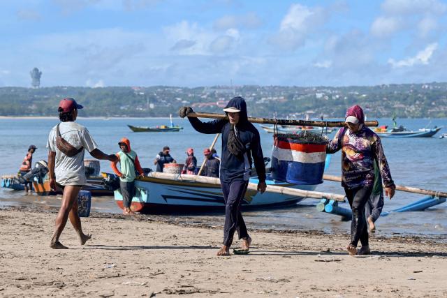 Workers carry fish after fishermen unloaded their catch from boats at Kedonganan beach near Denpasar on Indonesia's resort island of Bali on April 10, 2026. (Photo by SONNY TUMBELAKA / AFP)