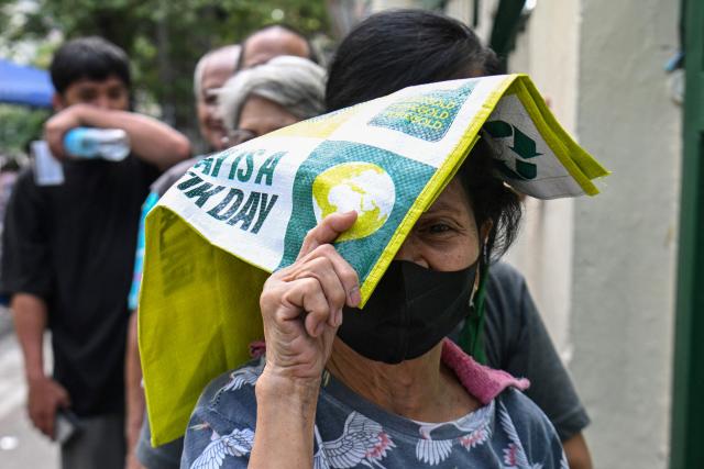 An elderly woman covers her head from while waiting in a queue outside a government-sponsored rolling store selling cheap rice near a public market in Manila on April 10, 2026. (Photo by Ted ALJIBE / AFP)