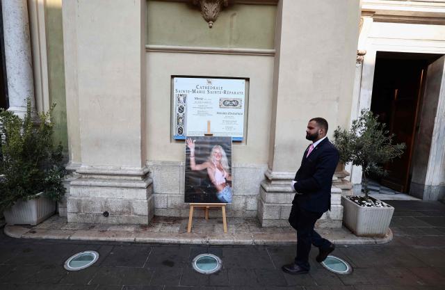 A man walks past a photograph depicting the first TV reality show star Loana Petrucciani waving to fans onboard a car on the Grande Armee avenue on July 5, 2001 on the last evening on the Loft Story TV broadcast, displayed ahead of her funeral ceremony in front of the church of Sainte-Reparate in Nice, southeastern France where she was found dead at her home at the age of 48, on April 10, 2026. (Photo by Thibaud MORITZ / AFP)