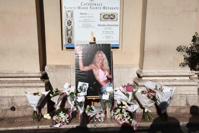 This photograph depicting the first TV reality show star Loana Petrucciani waving to fans onboard a car on the Grande Armee avenue on July 5, 2001 on the last evening on the Loft Story TV broadcast, is displayed with bunches of flowers ahead of her funeral ceremony in front of the cathedral of Sainte-Reparate in Nice, southeastern France where she was found dead at her home at the age of 48, on April 10, 2026. (Photo by Thibaud MORITZ / AFP)