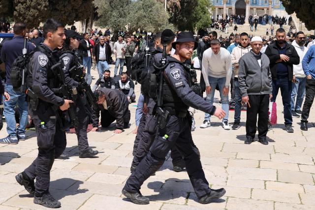 Israeli security walk past Muslim worshippers as they gather outside the Dome of the Rock at the Al-Aqsa Mosque compound for Friday noon prayers, in Jerusalem's Old City on April 10, 2026. The Al-Aqsa Mosque was reopened to Muslim worshippers on April 9, 2026, following a 40-day closure since the US-Israel war with Iran began on February 28. Jerusalem's Old City contains major holy sites for all three Abrahamic religions, which had been shuttered since the start of the war sparked by the US-Israeli attack on Iran. (Photo by AHMAD GHARABLI / AFP) / 