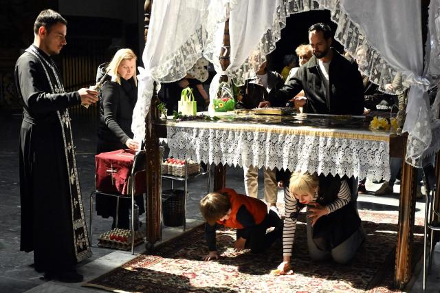 A woman and a child pass under a table symbolising the grave of Jesus Christ during a Good Friday service at the main Orthodox church St. Kliment of Ohrid in Skopje on April 10, 2026. The North Macedonian Orthodox Church celebrates Easter according to the Julian calendar. (Photo by Robert ATANASOVSKI / AFP)