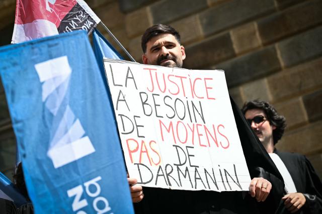 A lawyer holds a placard reading "Justice needs ressources not Darmanin" during a gathering in front of the Parlement of Brittany building as part of a national strike against a bill on criminal justice and respect for victims, in Rennes, western France, on April 10, 2026. (Photo by Lou BENOIST / AFP)