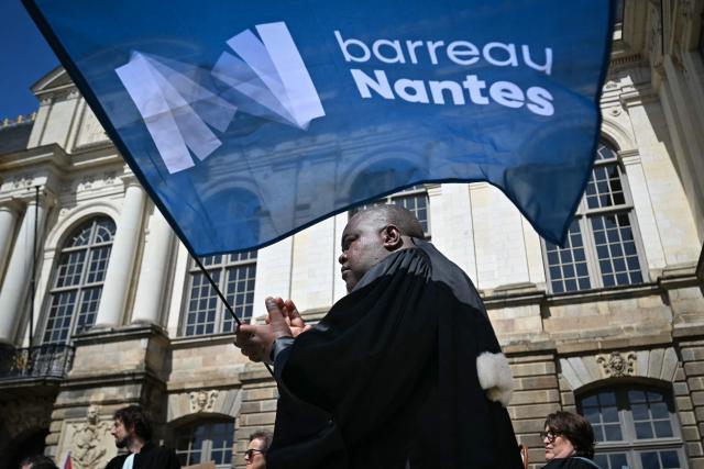 A lawyer holds a flag of the "Nantes Bar" during a gathering in front of the Parlement of Brittany building as part of a national strike against a bill on criminal justice and respect for victims, in Rennes, western France, on April 10, 2026. (Photo by Lou BENOIST / AFP)