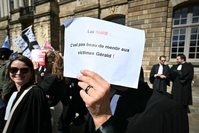 A lawyer holds a sign reading "SURE law: It's not nice to lie to victims Gerald!" during a gathering in front of the Parlement of Brittany building as part of a national strike against a bill on criminal justice and respect for victims, in Rennes, western France, on April 10, 2026. (Photo by Lou BENOIST / AFP)
