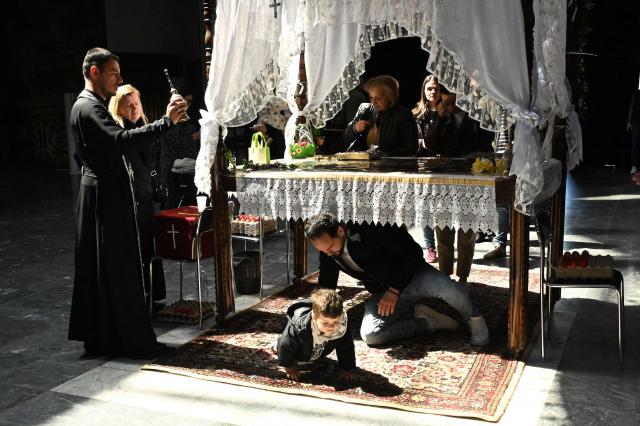 A man an child pass under a table  symbolising the grave of Jesus Christ during a Good Friday service at the main Orthodox church St. Kliment of Ohrid in Skopje on April 10, 2026. The North Macedonian Orthodox Church celebrates Easter according to the Julian calendar. (Photo by Robert ATANASOVSKI / AFP)