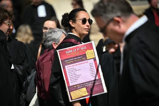 A lawyer holds a sign mimicking a menu with price compensations for victims of various crimes during a gathering in front of the Parlement of Brittany building as part of a national strike against a bill on criminal justice and respect for victims, in Rennes, western France, on April 10, 2026. (Photo by Lou BENOIST / AFP)
