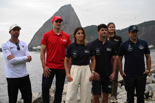 (L to R) US Taylor Canfield, Spain’s Diego Botin, Brazil’s Martine Grael, Brazil’s Marco Grael, Denmark’s Kahena Kunze, and France’s Quentin Delapierre pose for a picture at the Guanabara bay, with the Sugar Loaf mountain in the background, at the location of the Rio 2026 SailGP race in Rio de Janeiro, on April 10, 2026. (Photo by MAURO PIMENTEL / AFP)