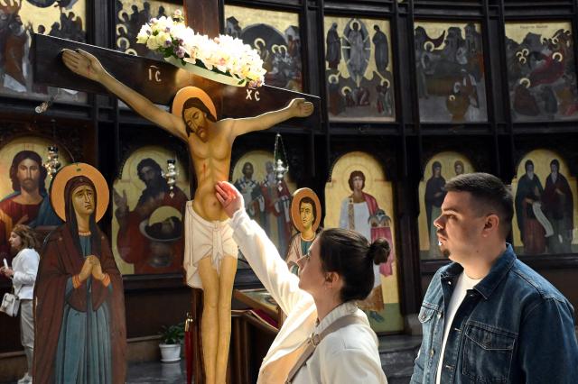 A faithful touches a wooden statue of Jesus  Christ during a Good Friday service at the main Orthodox church St. Kliment of Ohrid in Skopje on April 10, 2026. The North Macedonian Orthodox Church celebrates Easter according to the Julian calendar. (Photo by Robert ATANASOVSKI / AFP)