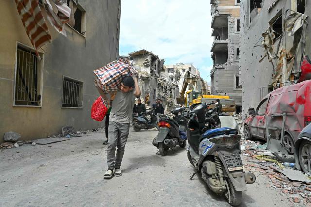 This photograph taken on April 10, 2026, during a media tour organized by Hezbollah’s media office shows residents carrying salvaged belognings at southern Beirut's Chweifat-Amrousiyeh neighbourhood that was targetted in an Israeli strike earlier this week. The Israeli military said on April 10 that it had "dismantled" more than 4,300 Hezbollah sites in Lebanon since fighting with the militant group began last month. (Photo by FADEL itani / AFP) / 