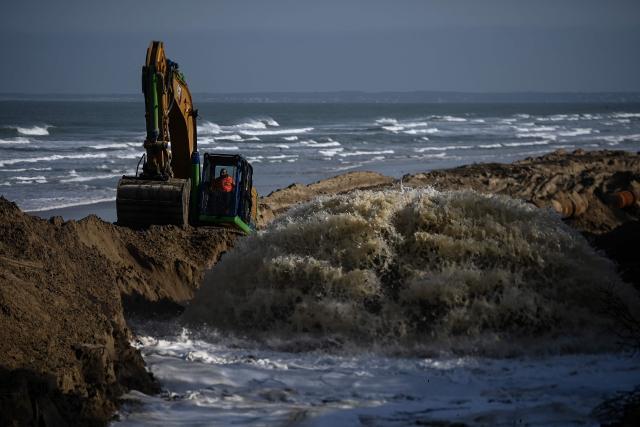 This photograph shows a mix of sand and water flowing out of a pipe at the site of a resanding operation where sand collected by a tanker from the sea bottom at the mouth of the Gironde estuary is brought through the pipe and spread on the beach, in Soulac-sur-Mer, south-western France, on April 10, 2026. An impressive network of pipes on the south beach of Soulac-sur-Mer sprayed a mixture of sand and water transported by ships from the Gironde estuary, as part of a large-scale experiment to combat coastal erosion. The stated objective is to inject some 200,000 cubic meters of sand along a one-kilometer stretch, at a time when the coastline in this area is receding by up to eight meters per year and this seaside resort is losing between 300,000 and 400,000 cubic meters of sand annually. (Photo by Christophe ARCHAMBAULT / AFP)