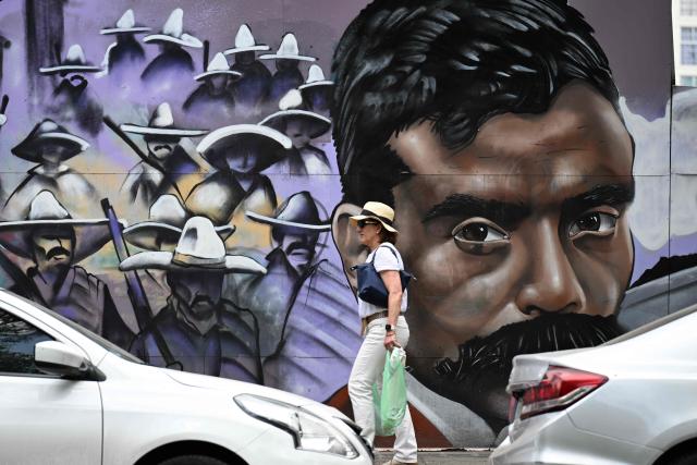 A woman walks past a mural by Kolore Fuentes depicting the iconic hero of the Mexican Revolution, Emiliano Zapata in Mexico City on April 10, 2026. Mexico commemorates the 107th anniversary of Zapata's death. (Photo by Yuri CORTEZ / AFP)