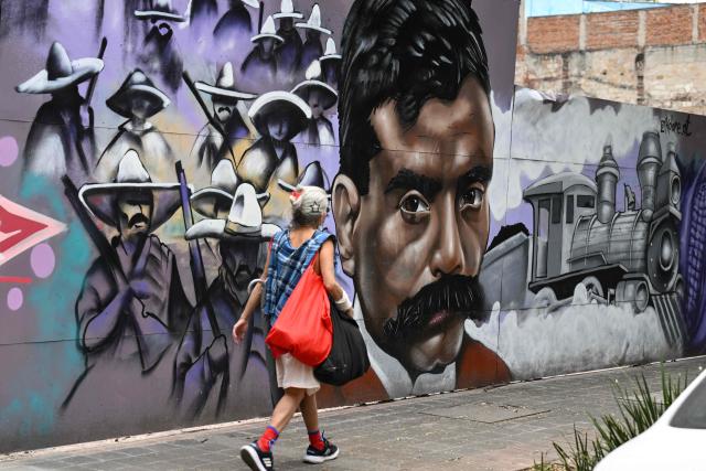 A woman walks past a mural by Kolore Fuentes depicting the iconic hero of the Mexican Revolution, Emiliano Zapata in Mexico City on April 10, 2026. Mexico commemorates the 107th anniversary of Zapata's death. (Photo by Yuri CORTEZ / AFP)