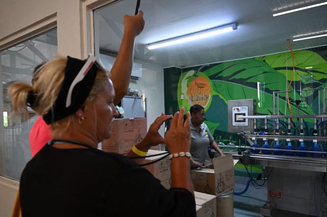 Tourists take snapshots while visiting The Curacao Liqueur Distillery in Willemstad, Curacao, in the Dutch Caribbean, on April 9, 2026. The iconic blue color of Curaзao liquor is not natural; it is obtained by adding a coloring agent designed to evoke the turquoise waters of the island’s idyllic Caribbean beaches. (Photo by Raul ARBOLEDA / AFP)