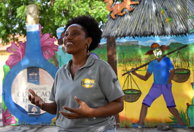 Tourist guide Genesis Riley explains the liquor production process to tourists at The Curacao Liqueur Distillery in Willemstad, Curacao, in the Dutch Caribbean, on April 9, 2026. The iconic blue color of Curaзao liquor is not natural; it is obtained by adding a coloring agent designed to evoke the turquoise waters of the island’s idyllic Caribbean beaches. (Photo by Raul ARBOLEDA / AFP)