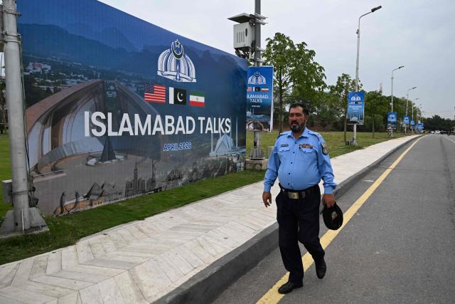 A police officer walks past a billboard for the US–Iran peace talks in Islamabad on April 11, 2026. US Vice President JD Vance was en route to Islamabad on April 11 for talks with Iran that the Pakistani premier hosting the warring sides called a "make or break" effort to permanently halt weeks of fighting in the Middle East. (Photo by Aamir QURESHI / AFP)