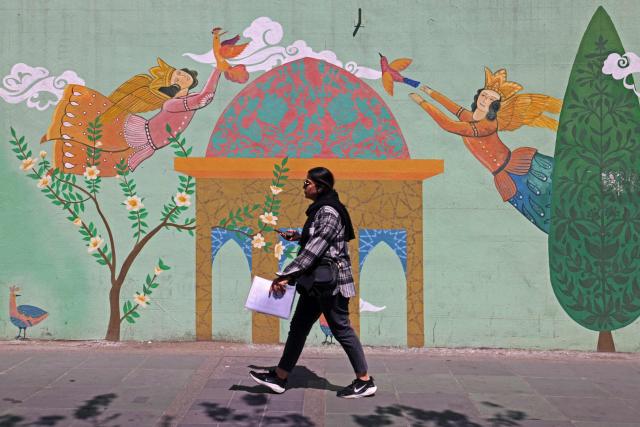 A woman walks past a wall mural along the roadside in Tehran on April 11, 2026. An Iranian government delegation met Pakistan's prime minister on April 11 to discuss the terms of planned "make or break" negotiations to end the Middle East war with a US party led by Vice President JD Vance. (Photo by ATTA KENARE / AFP) / 