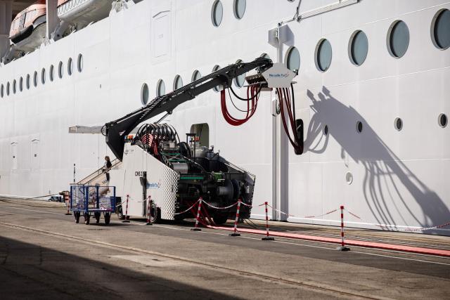 This photograph shows the MSC World Europa cruise boat moored at the Marseille cruise terminal while being charged using a "Cable Management System" at the Grand Port Maritime de Marseille, in Marseille, south-eastern France on April 11, 2026. Those systems allow boats to turn their engine off during their stay in Marseille harbour and to be charged by electricity. This new facilities are able to connect simultaneously three large cruise ships via electrical connection aiming to reduce smoke, vibrations and noise pollution in the city center. (Photo by CLEMENT MAHOUDEAU / AFP)