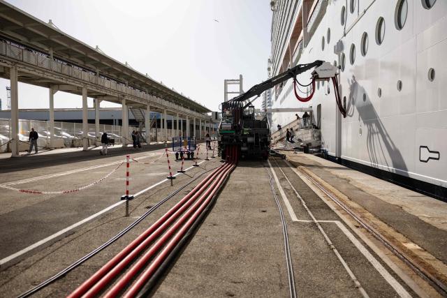 This photograph shows the MSC World Europa cruise boat moored at the Marseille cruise terminal while being charged using a "Cable Management System" at the Grand Port Maritime de Marseille, in Marseille, south-eastern France on April 11, 2026. Those systems allow boats to turn their engine off during their stay in Marseille harbour and to be charged by electricity. This new facilities are able to connect simultaneously three large cruise ships via electrical connection aiming to reduce smoke, vibrations and noise pollution in the city center. (Photo by CLEMENT MAHOUDEAU / AFP)