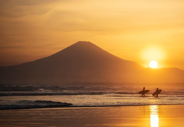 TOPSHOT - Surfboarders leave the water as the sunsets behind Mt. Fuji at the Katase Nishihama beach in Fujisawa, Kanagawa Prefecture on April 11, 2026. (Photo by Andrew CABALLERO-REYNOLDS / AFP)