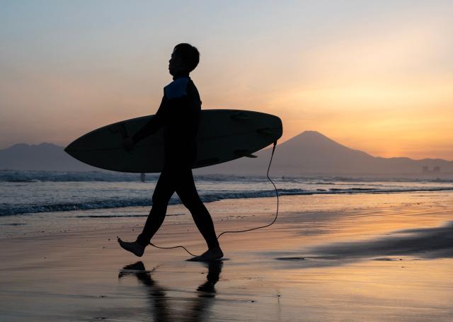 A surf boarder enters the water as the sunsets behind Mt. Fuji at the Katase Nishihama beach in Fujisawa, Kanagawa Prefecture on April 11, 2026. (Photo by Andrew CABALLERO-REYNOLDS / AFP)