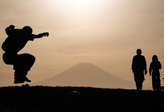 A skteboarder does a kickflip as a couple walks past, with Mt. Fuji in the background, near the Katase Nishihama beach in Fujisawa, Kanagawa Prefecture on April 11, 2026. (Photo by Andrew CABALLERO-REYNOLDS / AFP)