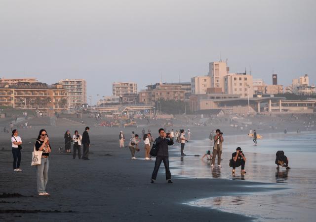 People stop to take sunset photos of Mt. Fuji at the Katase Nishihama beach in Fujisawa, Kanagawa Prefecture on April 11, 2026. (Photo by Andrew CABALLERO-REYNOLDS / AFP)