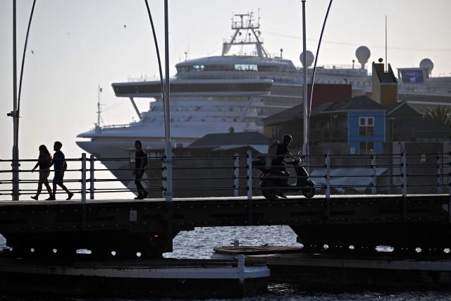 Tourists walk with the Grand Princess cruise ship in the background at the colonial center in Willemstad, in the Dutch Caribbean, on April 10, 2026. (Photo by Raul ARBOLEDA / AFP)