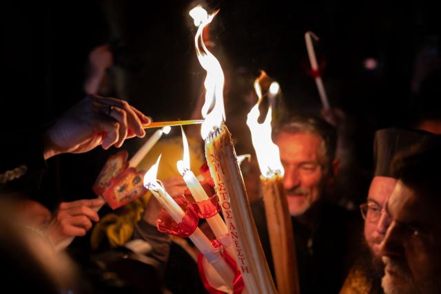 Greek Orthodox worshippers light candles with the Holy Fire during the Holy Saturday procession at the Church of the Holy Unmercenary Healers of Kolokynthis in Athens, on April 11, 2026. The Holy Fire, retrieved earlier in the day by a Greek government delegation from the Church of the Holy Sepulchre in Jerusalem under heightened security due to the ongoing conflict in the Middle East, arrived at Athens International Airport in the early evening before being distributed to churches across Greece ahead of Orthodox Easter Sunday on April 12. (Photo by Aggelos NAKKAS / AFP)