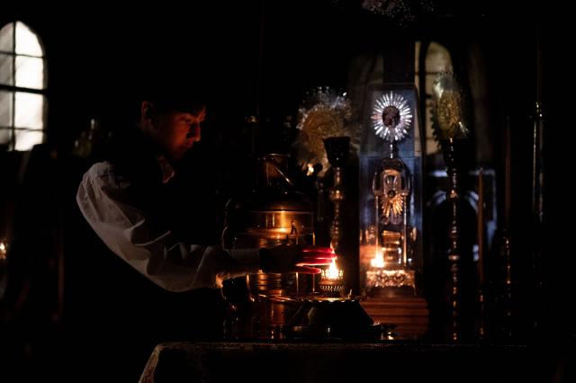 A Orthodox Christian touches the Holy fire during the Holy Saturday procession at the Church of the Holy Unmercenary Healers of Kolokynthis in Athens, on April 11, 2026. The Holy Fire, retrieved earlier in the day by a Greek government delegation from the Church of the Holy Sepulchre in Jerusalem under heightened security due to the ongoing conflict in the Middle East, arrived at Athens International Airport in the early evening before being distributed to churches across Greece ahead of Orthodox Easter Sunday. (Photo by Aggelos NAKKAS / AFP)