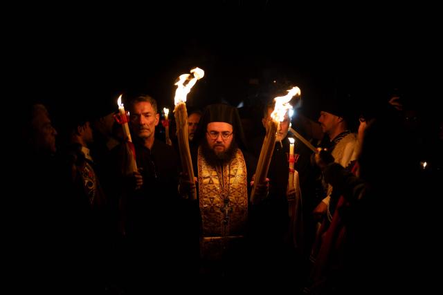 Greek Orthodox worshippers light candles with the Holy Fire during the Holy Saturday procession at the Church of the Holy Unmercenary Healers of Kolokynthis in Athens, on April 11, 2026. The Holy Fire, retrieved earlier in the day by a Greek government delegation from the Church of the Holy Sepulchre in Jerusalem under heightened security due to the ongoing conflict in the Middle East, arrived at Athens International Airport in the early evening before being distributed to churches across Greece ahead of Orthodox Easter Sunday. (Photo by Aggelos NAKKAS / AFP)