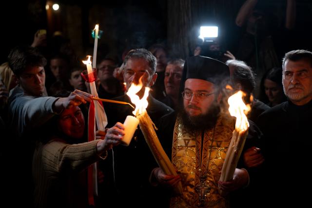 Greek Orthodox worshippers light candles with the Holy Fire during the Holy Saturday procession at the Church of the Holy Unmercenary Healers of Kolokynthis in Athens, on April 11, 2026. The Holy Fire, retrieved earlier in the day by a Greek government delegation from the Church of the Holy Sepulchre in Jerusalem under heightened security due to the ongoing conflict in the Middle East, arrived at Athens International Airport in the early evening before being distributed to churches across Greece ahead of Orthodox Easter Sunday. (Photo by Aggelos NAKKAS / AFP)