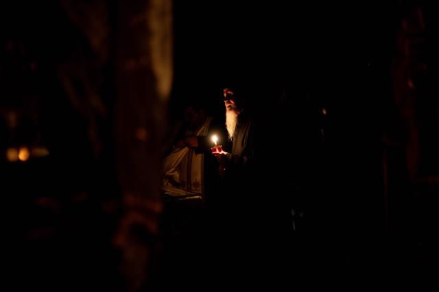 Greek Orthodox worshippers light candles with the Holy Fire during the Holy Saturday procession at the Church of the Holy Unmercenary Healers of Kolokynthis in Athens, on April 11, 2026. The Holy Fire, retrieved earlier in the day by a Greek government delegation from the Church of the Holy Sepulchre in Jerusalem under heightened security due to the ongoing conflict in the Middle East, arrived at Athens International Airport in the early evening before being distributed to churches across Greece ahead of Orthodox Easter Sunday. (Photo by Aggelos NAKKAS / AFP)