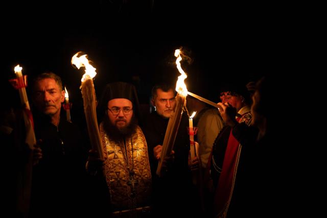 Greek Orthodox worshippers light candles with the Holy Fire during the Holy Saturday procession at the Church of the Holy Unmercenary Healers of Kolokynthis in Athens, on April 11, 2026. The Holy Fire, retrieved earlier in the day by a Greek government delegation from the Church of the Holy Sepulchre in Jerusalem under heightened security due to the ongoing conflict in the Middle East, arrived at Athens International Airport in the early evening before being distributed to churches across Greece ahead of Orthodox Easter Sunday. (Photo by Aggelos NAKKAS / AFP)