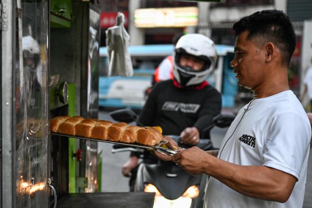 A man carries trays of the popular breakfast roll 'pandesal' to sell in Makati, Metro Manila on April 7, 2026. Rising liquefied petroleum gas prices are squeezing the already thin margins of Filipino street food vendors, forcing many to absorb costs to keep prices steady in fears of losing customers, while others raise prices or use minimal flames in cooking to stay afloat. While sticker shock at petrol stations has garnered the biggest headlines since the war in the Middle East forced the partial closure of the Strait of Hormuz, the rising price of LPG has hit the import-dependent archipelago's humble street food vendors hard. (Photo by Jam STA ROSA / AFP) / TO GO WITH AFP STORY: Iran-War-US-Israel-Philippines-economy-LPG, by Pam CASTRO