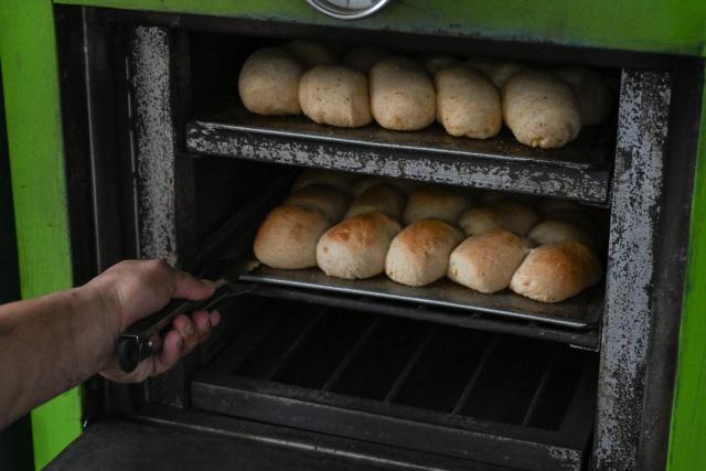 A man bakes trays of the popular breakfast roll 'pandesal' to sell in Manila on April 7, 2026. While sticker shock at petrol stations has garnered the biggest headlines since the war in the Middle East forced the partial closure of the Strait of Hormuz, the rising price of LPG has hit the import-dependent archipelago's humble street food vendors hard. (Photo by Jam STA ROSA / AFP) / TO GO WITH AFP STORY: Iran-War-US-Israel-Philippines-economy-LPG, by Pam CASTRO