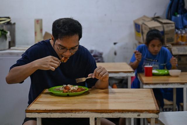 People eat at a curbside canteen in Manila on April 7, 2026. While sticker shock at petrol stations has garnered the biggest headlines since the war in the Middle East forced the partial closure of the Strait of Hormuz, the rising price of LPG has hit the import-dependent archipelago's humble street food vendors hard. (Photo by Jam STA ROSA / AFP) / TO GO WITH AFP STORY: Iran-War-US-Israel-Philippines-economy-LPG, by Pam CASTRO