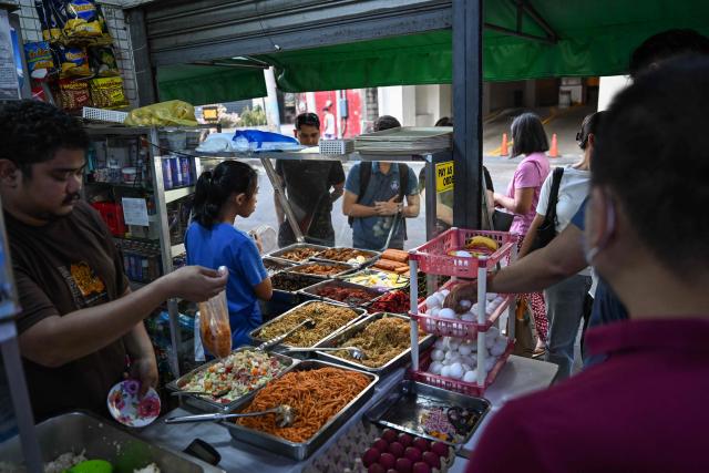 People buy food at a curbside canteen in Manila on April 7, 2026. While sticker shock at petrol stations has garnered the biggest headlines since the war in the Middle East forced the partial closure of the Strait of Hormuz, the rising price of LPG has hit the import-dependent archipelago's humble street food vendors hard. (Photo by Jam STA ROSA / AFP) / TO GO WITH AFP STORY: Iran-War-US-Israel-Philippines-economy-LPG, by Pam CASTRO