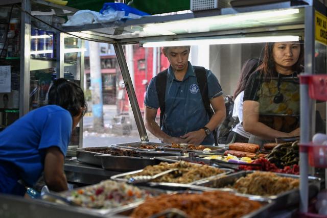 People buy food at a curbside canteen in Manila on April 7, 2026. While sticker shock at petrol stations has garnered the biggest headlines since the war in the Middle East forced the partial closure of the Strait of Hormuz, the rising price of LPG has hit the import-dependent archipelago's humble street food vendors hard. (Photo by Jam STA ROSA / AFP) / TO GO WITH AFP STORY: Iran-War-US-Israel-Philippines-economy-LPG, by Pam CASTRO