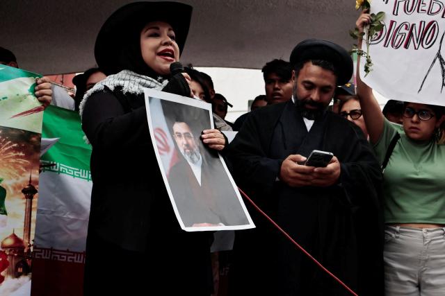 A demonstrator holds a portrait of Iranian supreme leader Mojtaba Khamenei as she speaks during a protest in support of Iran outside the Iranian embassy in Mexico City on April 11, 2026. (Photo by Josue PEREZ / AFP)