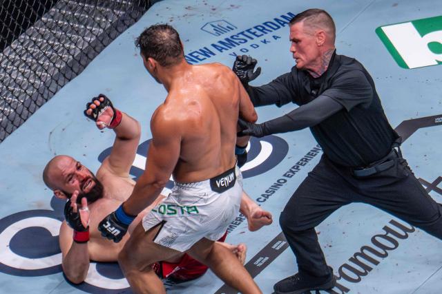 A referee moves in to stop Brazilian Light Heavyweight Paulo Costa (C) as previously undefeated Russian Azamat Murzakanov falls with a Technical Knock Out (TKO) during UFC 327 at Kaseya Center in Miami, on April 11, 2026. (Photo by Jim WATSON / AFP)