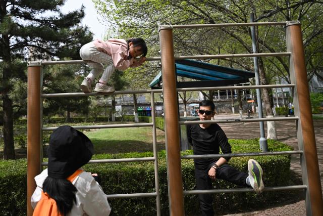 A man stretches next to a child climbing on exercise bars at a public park in Beijing on April 12, 2026. (Photo by Pedro PARDO / AFP)