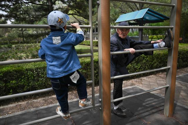 An elderly man stretches next to a child at a public park in Beijing on April 12, 2026. (Photo by Pedro PARDO / AFP)